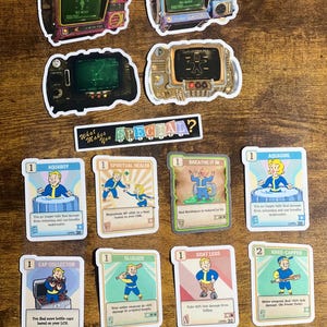 Puede incluir: Una colección de pegatinas y cartas coleccionables con diseños retro-futuristas. Las pegatinas representan pantallas de televisión antiguas con varios gráficos. Las cartas coleccionables muestran personajes de dibujos animados con texto como "AQUABOY". Una pancarta dice "What Makes You SPECIAL?"