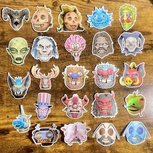 May include: A collection of colorful, whimsical stickers featuring various monster and creature designs. The stickers showcase a variety of faces, including demons, robots, and other fantastical characters, with detailed illustrations and vibrant colors.