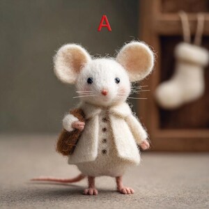Peut inclure: Une figurine de souris en feutre faite &agrave; la main, v&ecirc;tue d'un manteau cr&egrave;me et portant une sacoche marron. La souris a de grandes oreilles rondes, des joues roses et une longue queue rose. La lettre "A" est en rouge au-dessus de la souris.