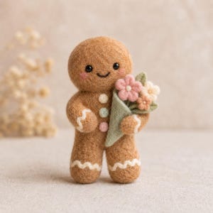 Könnte beinhalten: Handgefertigte Filzfigur eines lächelnden Lebkuchenmanns, der einen Strauß rosa und cremefarbener Blumen in einem grünen Kegel hält. Der Lebkuchenmann hat weiße Zuckergussdetails und pastellfarbene Knöpfe. Eine charmante Dekoration.