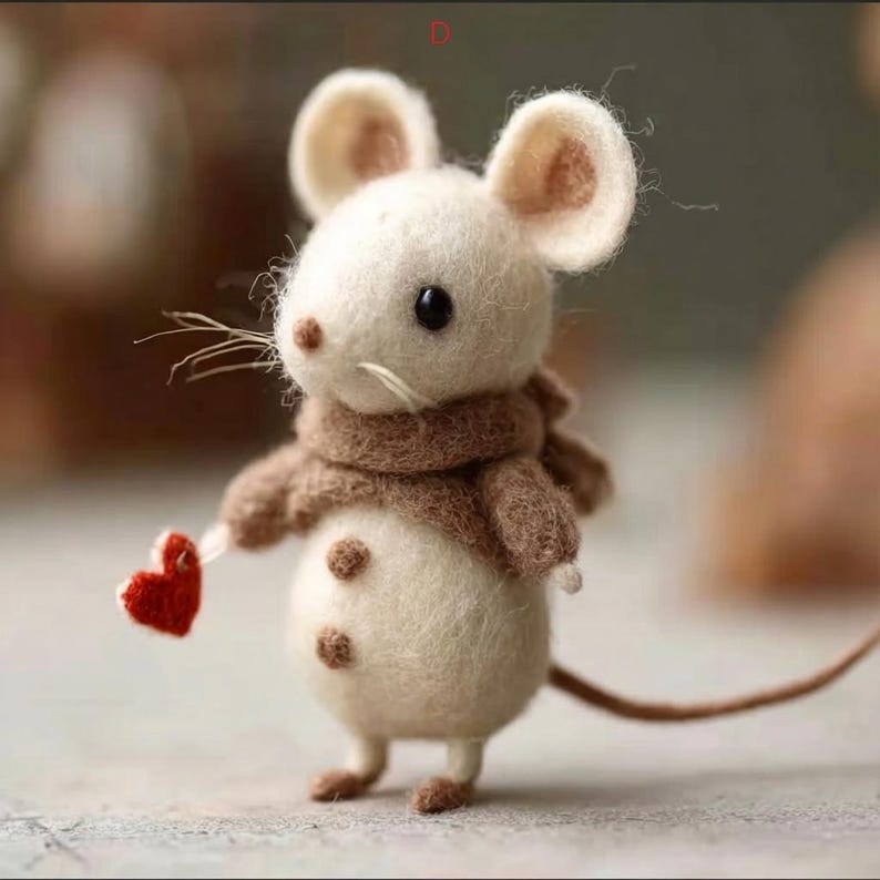 Peut inclure: Une figurine de souris en feutre faite &agrave; la main, avec un corps cr&egrave;me, de grandes oreilles et une &eacute;charpe marron. La souris tient un petit c&oelig;ur rouge. La figurine a une longue queue et de petits pieds bruns.