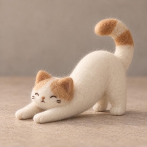 May include: A needle felted cat figurine in a stretching pose. The cat is primarily white with light orange patches on its ears and a matching orange-striped tail. It features embroidered eyes and whiskers, with a small brown nose.