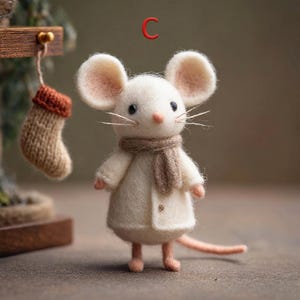 Peut inclure: Une figurine de souris en feutre blanc faite &agrave; la main, avec de grandes oreilles, un nez rose et des moustaches. La souris porte une &eacute;charpe beige et un manteau blanc. Une petite chaussette tricot&eacute;e est suspendue en arri&egrave;re-plan. La lettre "C" est au-dessus de la souris.