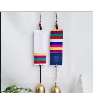 May include: Two hanging wind chimes with rectangular fabric panels and gold-colored bells. One panel is white with colorful stripes, the other is blue with colorful stripes. The bells hang from black cords.
