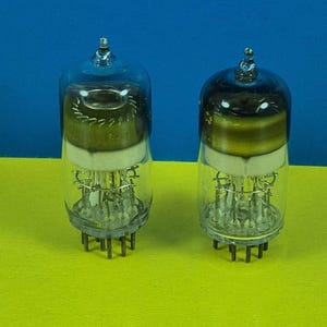 Pode incluir: Duas válvulas de vácuo vintage com invólucros de vidro transparente e componentes internos intrincados. Os tubos têm formato cilíndrico com topo arredondado e base com pinos. O fundo é azul e amarelo vibrantes.