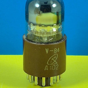 May include: A vintage vacuum tube with a brown base and a clear glass bulb. The bulb has a dark blue top and contains internal components. The base is marked with "V-84", a symbol, and "A 102". The tube has multiple pins at the bottom.