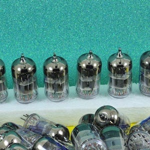 May include: A selection of vintage vacuum tubes, featuring silver tops and transparent glass bodies. Some are neatly arranged, others scattered below. The background is a teal-coloured surface.