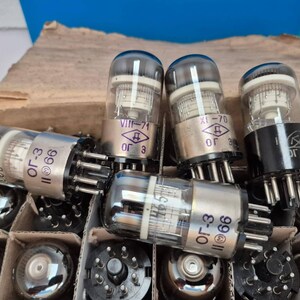 May include: A collection of vintage vacuum tubes, with clear glass bulbs and metallic bases, arranged in a cardboard box. The tubes have various markings, including "ОГ-3" and "11 66". Some tubes have the markings "VIII-71" and "XI-70".