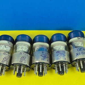 May include: Five vintage vacuum tubes with silver bases, clear glass bodies, and dark blue caps. Each tube has visible internal components and printed text, including "III-72", "IV-72", "VI-70", "VIII-70", and "XII 68". The background is yellow and blue.