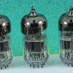 May include: A line of vintage vacuum tubes with clear glass casings and metallic tops. Each tube features internal components and pins at the base. The tubes are arranged in a row against a teal background.
