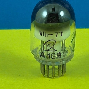 May include: A vintage vacuum tube with a clear glass bulb and a dark blue top. The tube has a white interior with the markings "VIII-77" and "A 169". The base has multiple metal pins. The background is yellow and blue.