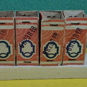 May include: Four vintage matchboxes are displayed. The boxes are orange with white stripes and blue and white label designs. Each box has the text "SH23П-EB". The boxes are on a white surface.