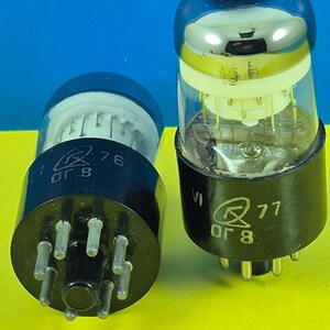 May include: Two vintage vacuum tubes with clear glass bulbs and black bases. One tube has the number "76" and the other has "77" printed on it. The tubes have multiple pins and internal components visible through the glass.