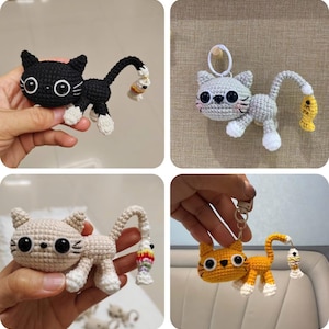 May include: Four crocheted cat keychains in various colors: black, gray, beige, and orange. Each cat has white paws and a tail with a fish attached. The keychains are handmade and feature detailed stitching and large, round eyes.