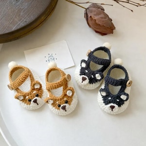 Può includere: Quattro paia di scarpine fatte a mano. Due paia sono marroni e bianche con un design a forma di orsetto, e due paia sono nere e bianche con un design a forma di orsetto. Ogni scarpa ha una chiusura con bottone e un piccolo pompon bianco sopra.
