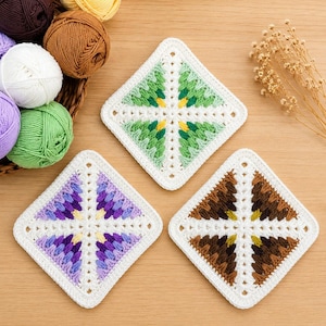 May include: Three square crochet coasters featuring a white border and a central diamond pattern. One coaster has green and yellow accents, one has purple and yellow, and one has brown and yellow. A basket of yarn balls sits nearby.