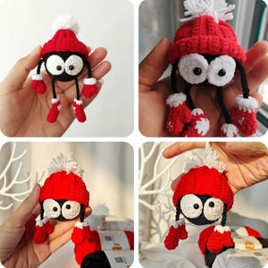 Może przedstawiać: Szydełkowa czarna figurka z dużymi białymi oczami, w czerwonej czapce z białym pomponem oraz pasującymi rękawiczkami i butami. Figurka ma czarne nogi i ramiona. Ręcznie robiony, fantazyjny przedmiot dekoracyjny.