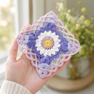 May include: A square crochet coaster featuring a central yellow circle surrounded by white petals, creating a daisy motif. The design is framed by layers of purple and light lavender yarn, finished with an intricate, openwork lattice border.