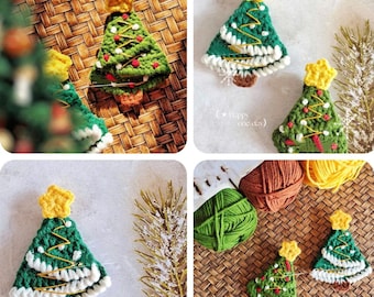 Puede incluir: Adornos de árbol de Navidad de ganchillo. Cada árbol es verde con ribete blanco, detalles rojos y blancos y una estrella amarilla en la parte superior. Los adornos se exhiben sobre una superficie tejida con hilo y vegetación.