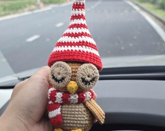 May include: A crocheted owl figurine wearing a red and white striped hat and scarf. The owl has large, round eyes and a yellow beak. The owl is wearing a red and white striped scarf and has a tan body.