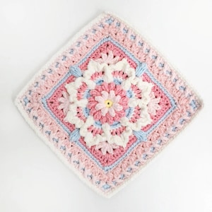 Könnte beinhalten: Ein quadratisches Häkelmotiv mit einem gelben Punkt in der Mitte, umgeben von Schichten aus rosa, weißem und hellblauem Garn. Das Design enthält komplexe blütenartige Blütenblattmuster und strukturierte Maschen in symmetrischer Anordnung.