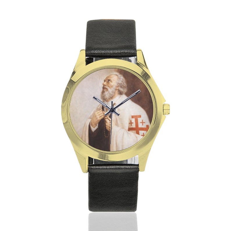 May include: Gold-tone wristwatch with a black leather band. The watch face features a portrait of a man with a white beard and a white robe with a red cross emblem. The watch has a gold bezel.