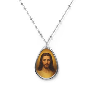 May include: Silver-toned necklace featuring a teardrop pendant with a portrait of Jesus. The portrait has a gold background and depicts Jesus with long brown hair and a light-colored robe. The chain is delicate and has small, round accents.