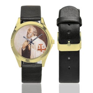 May include: Gold-tone wristwatch with a black leather band. The watch face features a portrait of a man in religious attire. The watch has a gold-colored bezel and black hands. The watch band is black leather.