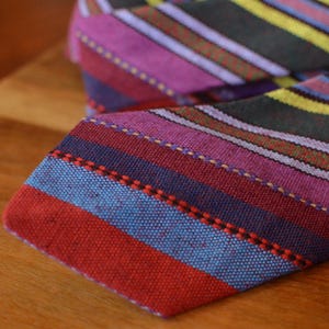 May include: A colorful necktie with a striped pattern in shades of red, blue, purple, yellow, and green. The tie is made of woven fabric and is folded over on a wooden surface.