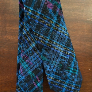 May include: A patterned necktie with a plaid design. The tie features a dark blue background with intersecting lines in teal, purple, and yellow. The tie is made of a woven fabric.