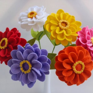 May include: A bouquet of felt flowers in a white vase. The flowers are red, yellow, white, purple, and orange. The flowers are all in bloom and have a realistic appearance.