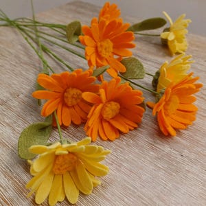 May include: A bouquet of felt flowers in shades of orange and yellow. The flowers have a daisy-like shape with multiple layers of petals.