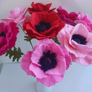 May include: A bouquet of felt flowers in shades of pink and red. The flowers have black centers and are arranged in a vase.