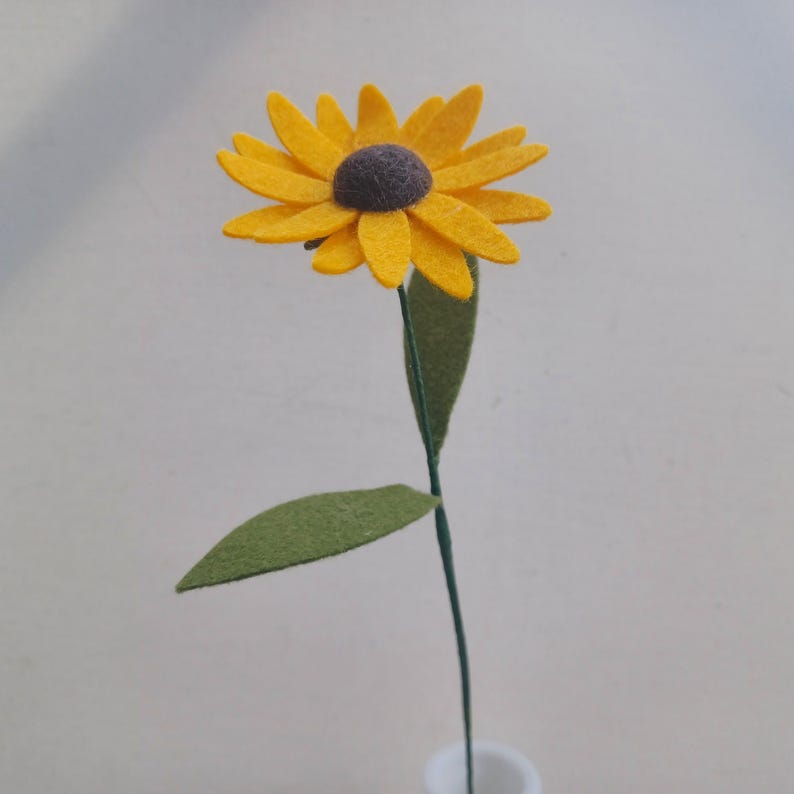 Op de afbeelding: Een enkele viltzonnebloem met een gele bloem en groene bladeren op een draadsteel.