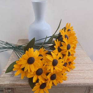Op de afbeelding: Een boeket van viltzonnebloemen in tinten geel en bruin. De bloemen zijn in een vaas gerangschikt en hebben groene stelen.