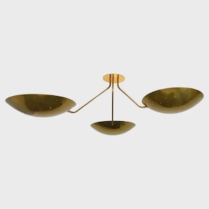 May include: A brass-toned ceiling light fixture with three bowl-shaped shades. The shades are perforated with small holes and are suspended from a central mounting plate by slender arms. The fixture has a mid-century modern aesthetic.