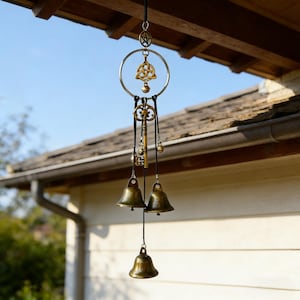 Peut inclure: Un carillon éolien décoratif avec des éléments en laiton. Il comprend une clé, des cloches et un cadre circulaire avec un nœud celtique et une étoile. Le carillon est suspendu à un cordon noir. Fond bleu et toit en bois.