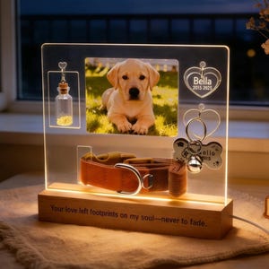 May include: A lighted memorial plaque with a photo of a yellow Labrador puppy. The plaque includes a dog collar, a heart-shaped tag, and a small bottle. The wooden base has the text "Your love left footprints on my soul—never to fade."
