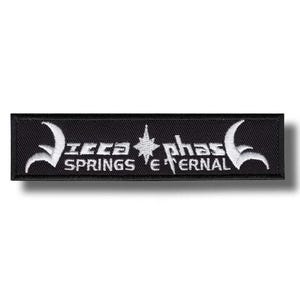Op de afbeelding: Zwart rechthoekig embleem met wit geborduurde tekst en ontwerpen. De tekst luidt "Icca Springs Eternal" met gestileerde graphics aan weerszijden en een ster in het midden. De patch is waarschijnlijk voor kleding of accessoires.