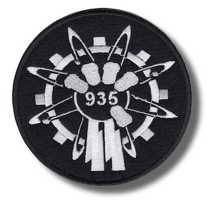 Può includere: Una toppa rotonda nera con un disegno ricamato bianco. Il disegno presenta un ingranaggio, forme stilizzate e il numero "935" al centro. La toppa è adatta per abbigliamento o accessori.