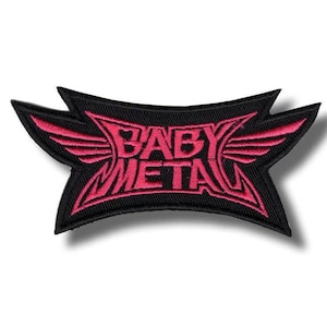 Puede incluir: Parche bordado negro con el texto "BABY METAL" en rosa, adornado con alas estilizadas. El parche tiene una forma angular distintiva, ideal para aplicar en ropa o accesorios.