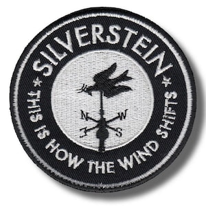 May include: Circular black and white embroidered patch with the text "SILVERSTEIN" and "THIS IS HOW THE WIND SHIFTS". The center features a weather vane design with a bird and compass points.