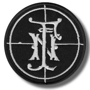 May include: A circular black patch with a white embroidered design. The design features the intertwined letters "F" and "N" within a white crosshair. The patch has a white border, possibly an emblem or logo.