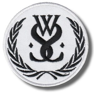 Puede incluir: Un parche redondo bordado en blanco con un diseño negro entrelazado de "W" y "S" en el centro. El diseño está rodeado por una corona de laurel negra. El parche tiene un borde blanco.