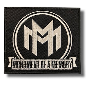 Puede incluir: Parche cuadrado negro con un diseño bordado en blanco. El diseño presenta dos letras "M" mayúsculas blancas estilizadas dentro de un círculo blanco. Debajo, una pancarta blanca con las palabras "MONUMENT OF A MEMORY" bordadas en blanco.