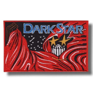 May include: Rectangular patch with the text "DARK STAR" in blue. The patch features a red and black design with a stylized figure, two yellow stars, and a white and black striped element.