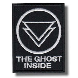 May include: Black rectangular patch with white embroidered design. The design features a circle with a downward-pointing triangle inside, and the text "THE GHOST INSIDE" below. The patch has a black border and is likely for clothing or accessories.