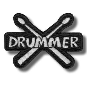 May include: Black and white embroidered patch featuring the word "DRUMMER" in white block letters. The text is set against a black rectangular background, with two crossed drumsticks in white behind it.