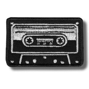 Op de afbeelding: Zwart en wit geborduurde patch met een cassettebandje ontwerp. De patch heeft een rechthoekige vorm met afgeronde hoeken. Het cassettebandje ontwerp is gedetailleerd met witte stiksels op een zwarte achtergrond.