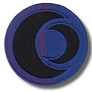 Puede incluir: Parche bordado redondo con un centro negro y un diseño exterior azul. El diseño azul presenta una forma de media luna estilizada y un círculo más pequeño. Las costuras rojas acentúan el borde azul.